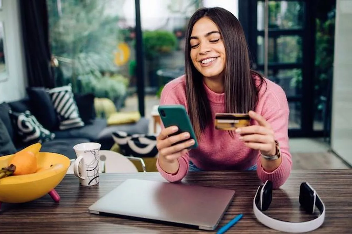 Mulher jovem usando cartão de crédito para fazer pagamento no celular