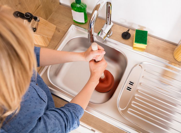 Mulher desntupindo a pia da cozinha