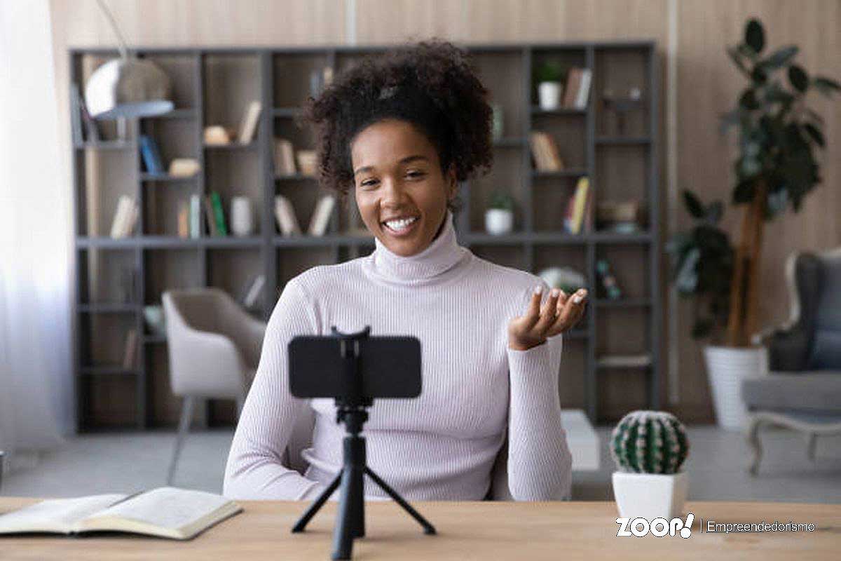 Uma mulher negra sorridente gravando um vídeo para ganhar mais inscritos no youtube.