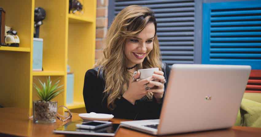 Mulher jovem estudando sobre rankear os Stories no Google usando um notebook enquanto segura uma xícara de café.