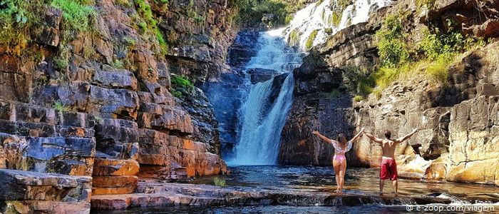 Duas pessoas com os braços erguidos olham para a Catarata dos Couros em Goiás