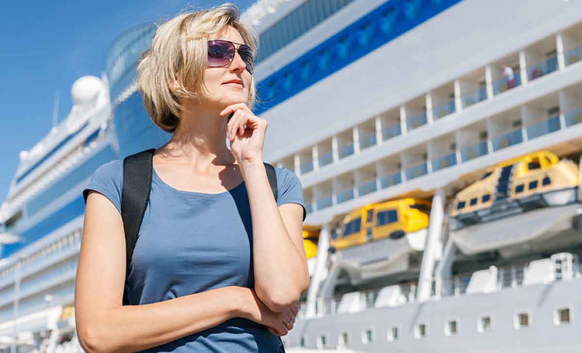 Mulher loira jovem posando para foto em frente a um navio de cruzeiro se preparando para sua viagem solo.