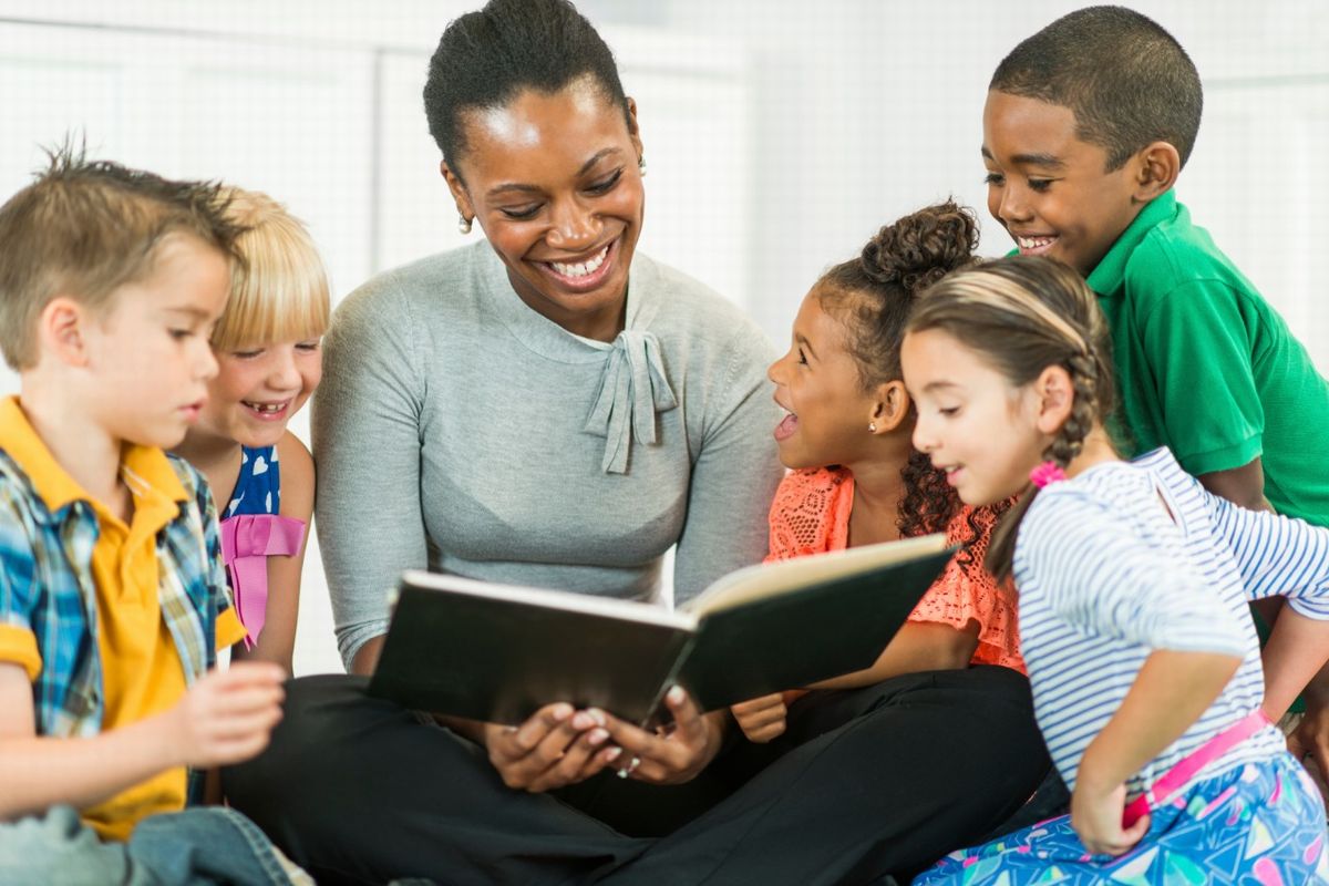 Uma professora lendo um livro enorme ilustra o nosso artigos sobre: Entenda a importância da leitura infantil